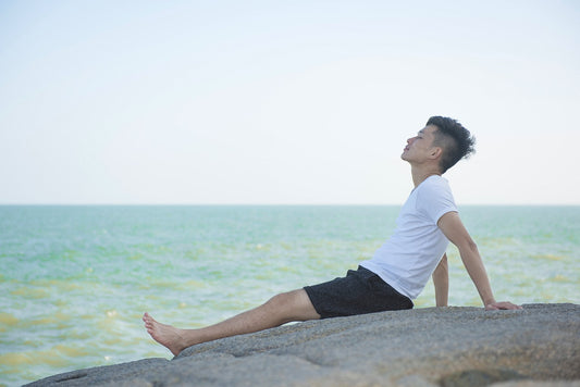 Junger Mann genießt, zurückgelehnt auf einem Stein sitzend, das türkise Meer