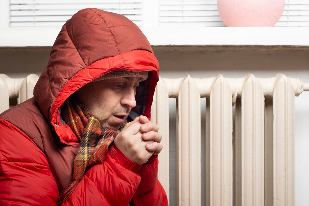 Mann mit einer Dicken Winterjacke vor einer Heizung