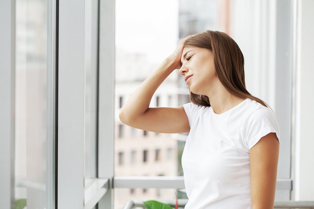 Frau am offenen Fenster mit Kopfschmerzen