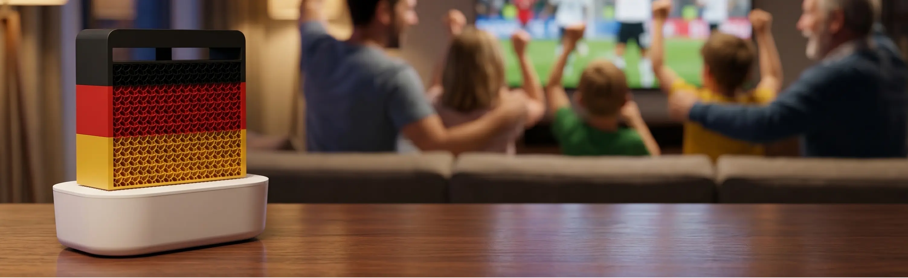 SalinoVatis WM Edition in den Farben der deutschen Flagge auf einem Wohnzimmerregal. Im Hintergrund eine Familie, die Fußball guckt.